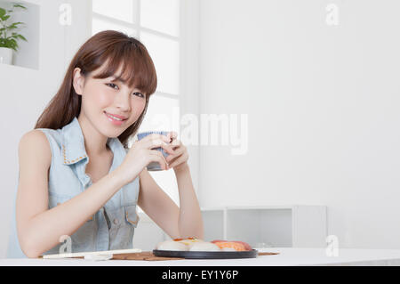 Junge Frau hält eine Teetasse und lächelt in die Kamera, Stockfoto