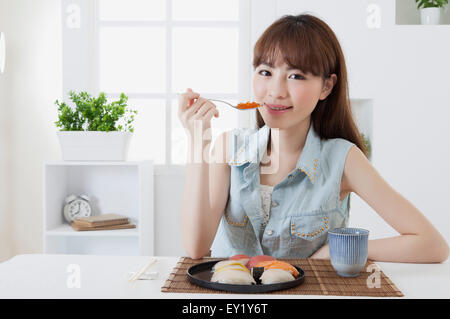 Junge Frau hält japanisches Essen und lächelt in die Kamera, Stockfoto