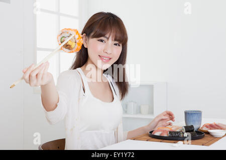 Junge Frau hält Sushi und lächelt in die Kamera, Stockfoto