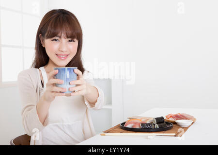 Junge Frau hält eine Teetasse und lächelt in die Kamera, Stockfoto