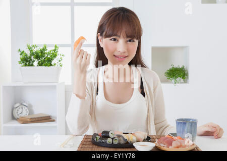 Junge Frau hält Sashimi und lächelt in die Kamera, Stockfoto