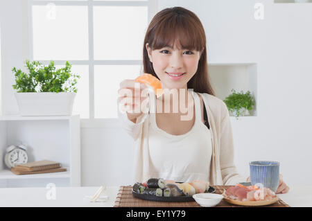 Junge Frau hält Sashimi und lächelt in die Kamera, Stockfoto