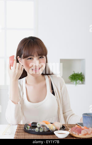 Junge Frau hält Sashimi und lächelt in die Kamera, Stockfoto