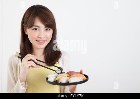 Junge Frau mit Stäbchen und einen Teller mit japanisches Essen mit Lächeln, Stockfoto