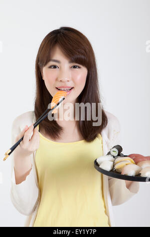 Junge Frau mit Stäbchen und einen Teller mit japanisches Essen mit Lächeln, Stockfoto