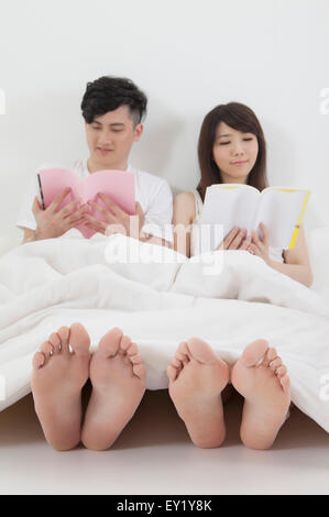 Junges Paar sitzt und liest Bücher über Bett, Stockfoto