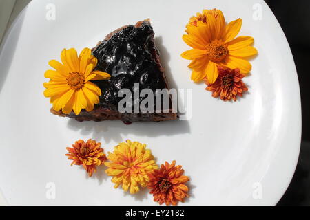 leichte vegetarische Torte mit Brombeermarmelade an der Spitze verziert leuchtend blühen Blumen Stockfoto