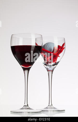 Weingläser mit roten Wein und Golf Ball auf weißen Tisch Stockfoto