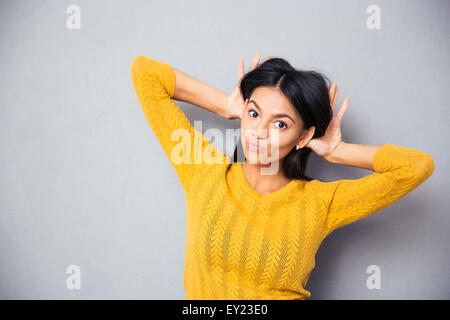 Porträt einer jungen Frau, die machen eines lustigen Gesicht auf grauem Hintergrund Stockfoto