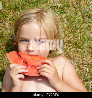 Porträt von kleines Kind blondes Mädchen mit Scheibe Wassermelone, liegen am grünen Rasen, Sommer, Entspannung Stockfoto