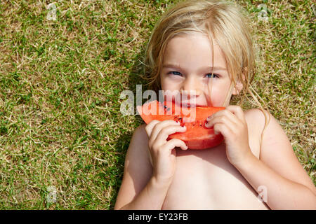 Porträt von kleines Kind blondes Mädchen mit Scheibe Wassermelone, liegen am grünen Rasen, Sommer, Entspannung Stockfoto