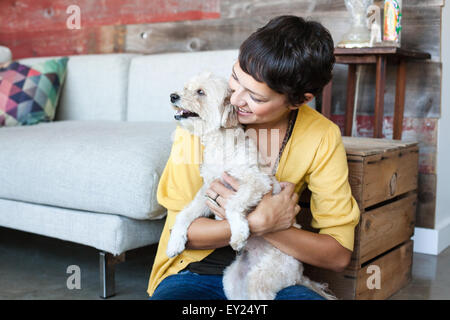 Junge Frau umarmt Hund am Boden des Wohnzimmers Stockfoto