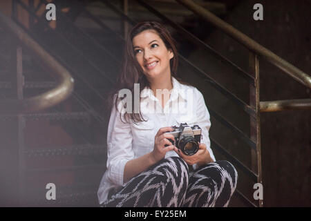 Junge Frau sitzt auf Schritte halten SLR Kamera Stockfoto