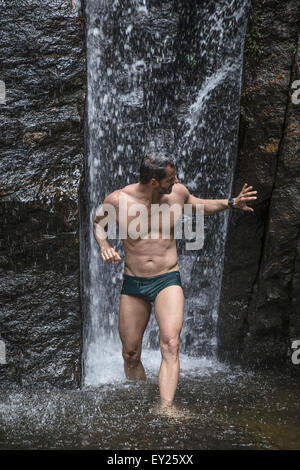 Reifer Mann berühren Felsen vor Wasserfall in Tijuca Wald, Rio De Janeiro, Brasilien Stockfoto