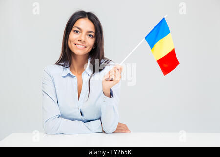 Lächelnde junge Frau sitzt am Tisch mit rumänische Flagge isoliert auf einem weißen Hintergrund. Blick in die Kamera Stockfoto