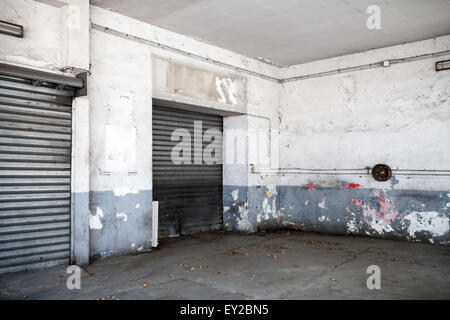 Abstrakte leere weiße innere alte Kfz Werkstatt mit Asphaltdecke und geschlossenen Metalltor Stockfoto