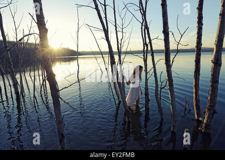 Eine Frau in einem weißen Kleid im seichten Wasser in der Abenddämmerung Stockfoto