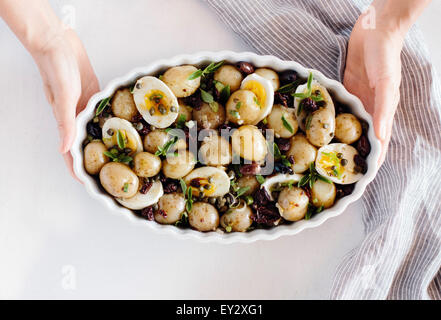 Baby-Kartoffel-Salat mit Sun-Dried Tomaten und Kapern Dressing wird in eine ovale weiße Schale serviert. Eine Frau ist es in der Hand hält. Stockfoto