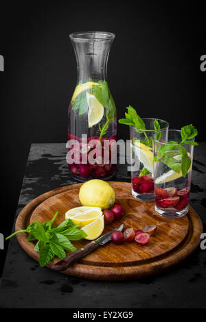 Wasserkrug mit frischen Früchten und Kräutern auf Schiefer Tisch mit Holzplatte Stockfoto