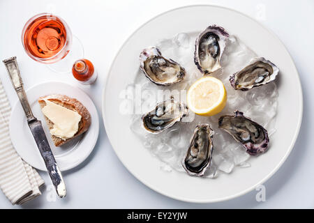 Austern auf weißen Teller, Rosé und dunkles Brot mit Butter auf weißem Hintergrund eröffnet Stockfoto