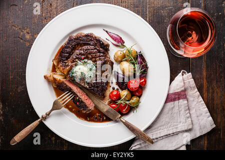 In Scheiben geschnitten mittlere seltene Gegrilltes Beefsteak Ribeye mit Kräuterbutter und Babykartoffeln und Wein auf weißen Teller auf hölzernen Hintergrund Stockfoto