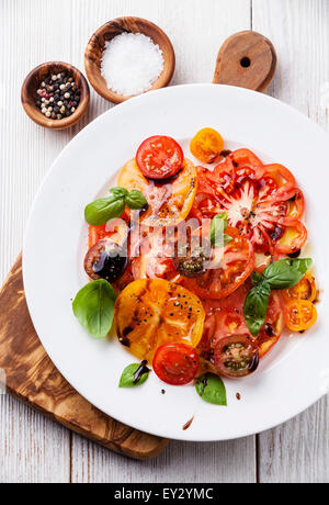 Reife frische bunte Tomaten Salat mit Olivenöl und Balsamico-Essig auf weißem Holz Hintergrund Stockfoto