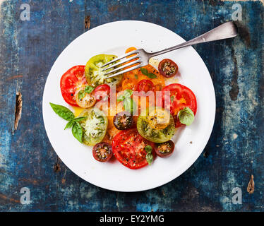 Reife frische bunte Tomaten Salat mit Olivenöl und Basilikum auf blauem Hintergrund aus Holz Stockfoto