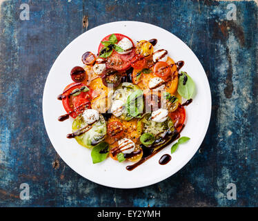 Bunte Tomaten-Salat mit Mozzarella und Balsamico-Essig auf blauem Hintergrund aus Holz Stockfoto