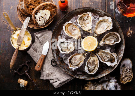 Austern auf Metall Kupferplatte mit dunklem Brot mit Butter und Rosé auf dunklem Holz eröffnet Stockfoto