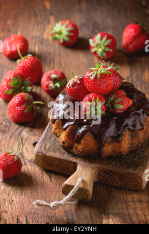 Hausgemachter Schokoladenkuchen mit Erdbeeren und dunkle Schokoladenganache auf kleinen Holzbrett über Holztisch serviert Stockfoto