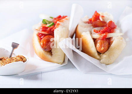 Hausgemachte Hot Dogs auf Backen Papper mit Tomatensauce, Zwiebel, Pfeffer und Senf auf hellblauem Hintergrund aus Holz. Stockfoto