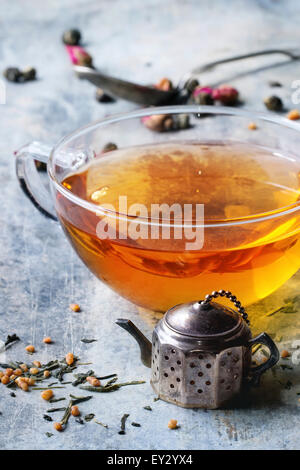 Vintage Teesieb Teekanne und Glas Tasse heißen Tee mit trockenen grünen Teeblätter. Alte Zinn Backgtound. Stockfoto