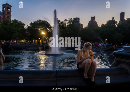 New York, NY - 20. Juli 2015 - eine Frau am Brunnen sitzt und untersucht ihr Handy an einem Sommerabend im Washington Square Park Stacy Walsh Rosenstock/ALamy Stockfoto