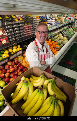 Ein Mann steht in einem Lebensmittelladen neben einem Display von frischem Obst und Gemüse. Stockfoto