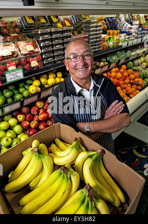 Ein Mann steht in einem Lebensmittelladen neben einem Display von frischem Obst und Gemüse. Stockfoto