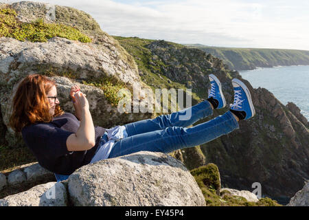 Junge Frau, die ein Bild von ihren Füßen am Portmehor Point, Carn Galver, Cornwall, UK Stockfoto