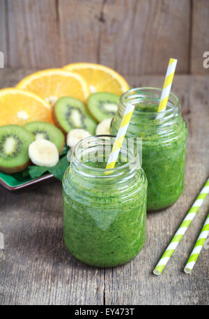 Gesunden grünen Smoothie aus Spinat, Kiwi, Bananen und Orangen in ein Gefäß mit grüne Strohhalme auf einem Holztisch hergestellt Stockfoto