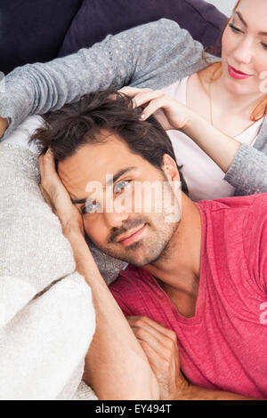 Junge Paar entspannen auf der Couch In the Living Room, mit nachdenklichen Gesichtsausdruck, während Freund ist liegend auf dem Schoß ihrer Freundin. Stockfoto