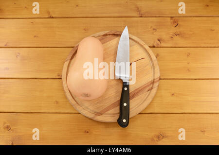 Ganze Butternut-Kürbis mit einem scharfen Küchenmesser auf einem Holzbrett Stockfoto