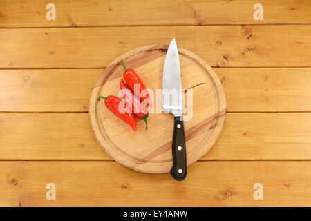 Drei helle rot Baby-Paprika mit einem scharfen Küchenmesser auf ein Schneidbrett aus Holz Stockfoto