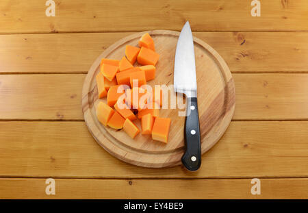 Stücke von gehackten Butternut-Kürbis mit einem scharfen Küchenmesser auf einem Holzbrett Stockfoto