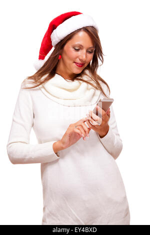 Kalten attraktive junge Frau mit einem süßen Lächeln in eine festliche rote Weihnachtsmütze schlürfen eine heiße Tasse Kaffee, die sie in ihr wiegt ist Stockfoto