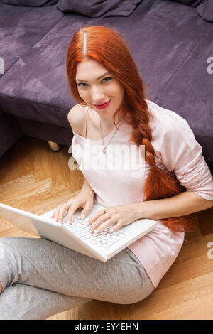 Hübsche junge Frau mit ihrem Laptop Computer In the Living Room mit Füßen auf dem Tisch und ernstem Gesicht zeigen. Stockfoto