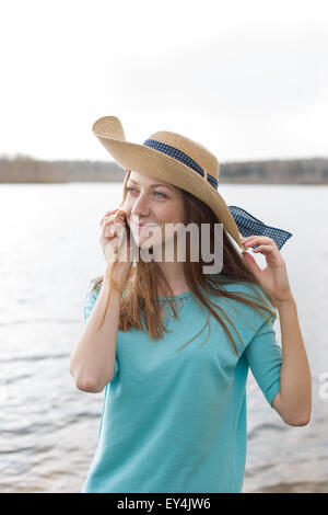 Sommersprossige Mädchen mit Hut lächelnd und hören Shell auf dem See bei windigem Wetter Stockfoto