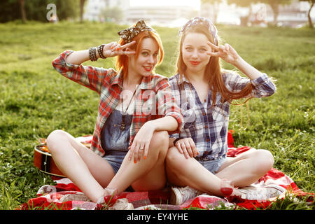 Zwei junge lächelnd Hipster Mädchen, die Spaß beim Picknick im Park in den Sonnenuntergang Stockfoto