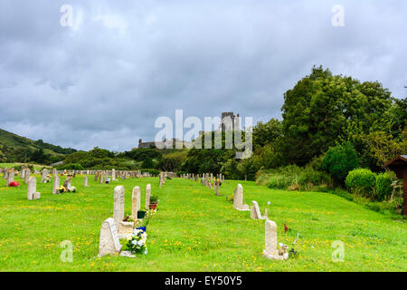 Friedhof Friedhof in Corfe Dorf mit Bäumen auf drei Seiten und in der Ferne die Ruinen von Corfe Castle. Dunkle schwere Gewitterwolken Overhead. Stockfoto