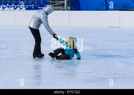 Nicht erkennbar, nicht identifizierte Mutter gibt eine helfende Hand für ihr Kind, das auf dem Eis eine Eisbahn stürzten. Stockfoto