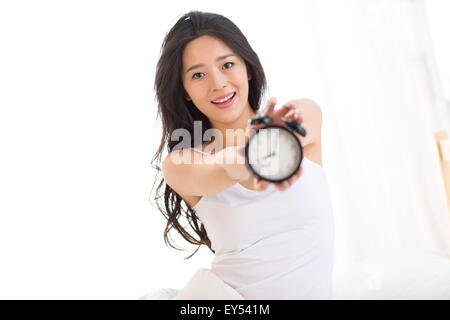 Junge Frau im Schlafzimmer halten Wecker Stockfoto