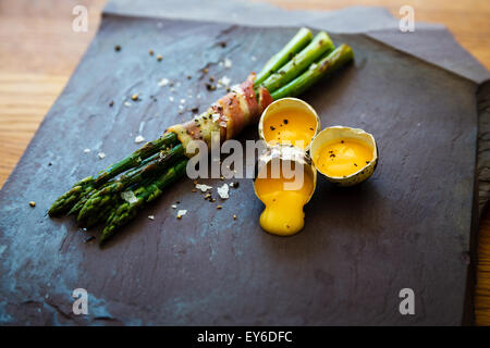 Lenguado, Bauchspeck umwickelt Spargel "Soldaten" mit Confit Wachtel Eigelb in ihren Schalen auf eine Platte aus Schiefer serviert. Stockfoto