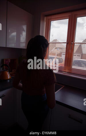 Silhouette einer jungen Frau, Blick durch ein Fenster blind, hintere Sicht. Stockfoto